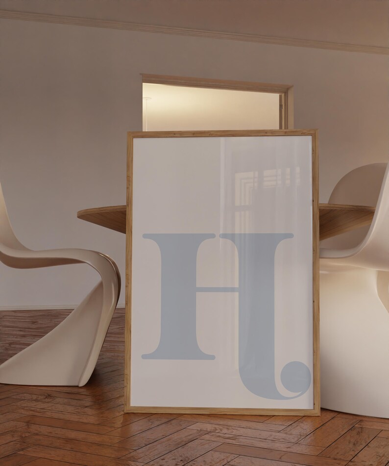 May include: A framed print featuring a light blue letter "H" on a white background. The frame is made of natural wood.