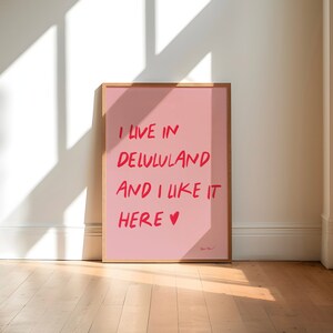 以下が含まれることがあります： 赤い文字で「I live in Lululand and I like it here &hearts;」と書かれたピンクのポスターが額縁に入っています。