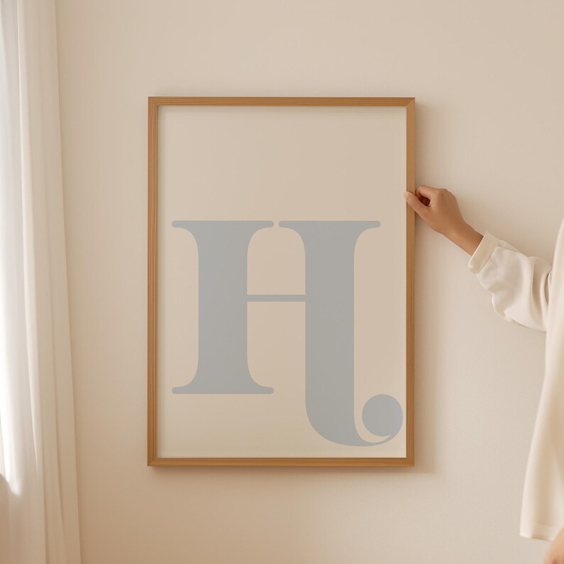 May include: A framed print featuring a large, light blue letter "H" in a simple, modern font. The frame is a light wood colour.