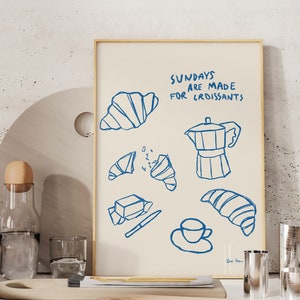 Op de afbeelding: Een blauwe en witte illustratie van een koffiepot, croissants, boter en een kopje koffie. De tekst luidt "Zondagen zijn gemaakt voor croissants".