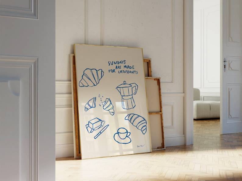 Op de afbeelding: Een wit ingelijst print met blauwe illustraties van croissants, boter, een koffiepot en een kopje koffie. De tekst op de print luidt "Zondagen zijn gemaakt voor croissants".