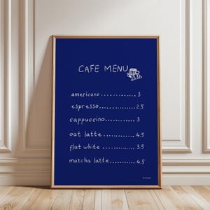 May include: A framed cafe menu with a navy blue background and white text. The menu lists coffee drinks such as americano, espresso, cappuccino, oat latte, flat white, and matcha latte. A small illustration of a coffee cup and croissant is in the top right corner.