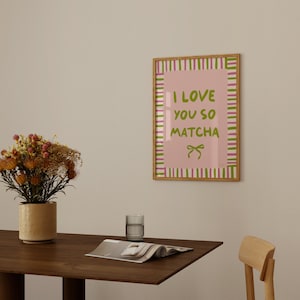 May include: A framed print with a pink background and green text that reads "I love you so matcha". The frame has a wooden border and a pink and green striped pattern.