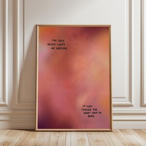 Könnte beinhalten: Ein rechteckiges Wandbild in einem dünnen Holzrahmen mit einem Farbverlauf in Orange, Pink und Dunkelrot. Der Text lautet: THE COLD NEVER LASTS MY DARLING und IT JUST TEACHES THE HEART HOW TO BURN in schwarzer Schrift auf dem Bild.