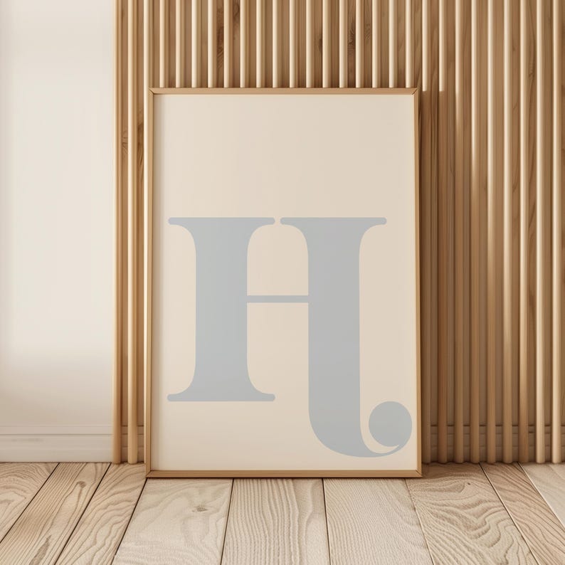 May include: A framed print featuring a light blue letter H on a cream background. The frame is a light wood colour.