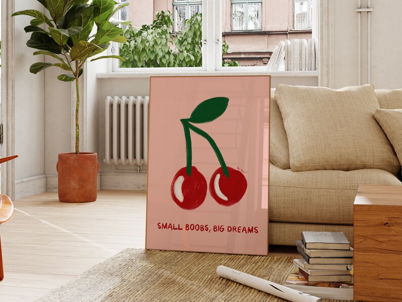 K&ouml;nnte beinhalten: Rosa-wei&szlig;er gerahmter Kunstdruck mit einer Zeichnung von zwei roten Kirschen mit gr&uuml;nen Stielen und Bl&auml;ttern. Der Text "SMALL BOOBS, BIG DREAMS" ist unter den Kirschen gedruckt.