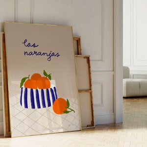 May include: A framed print with a light brown background featuring a blue and white striped bowl filled with orange oranges. The text "las naranjas" is written in black cursive above the bowl.