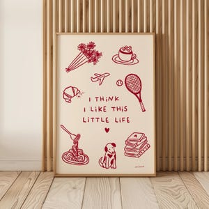 Puede incluir: Impresión artística enmarcada con dibujos lineales rojos sobre un fondo crema. Las ilustraciones incluyen un ramo, un cruasán, un avión, una raqueta de tenis, una taza de café, pasta, un perro, libros y el texto "I THINK I LIKE THIS LITTLE LIFE".