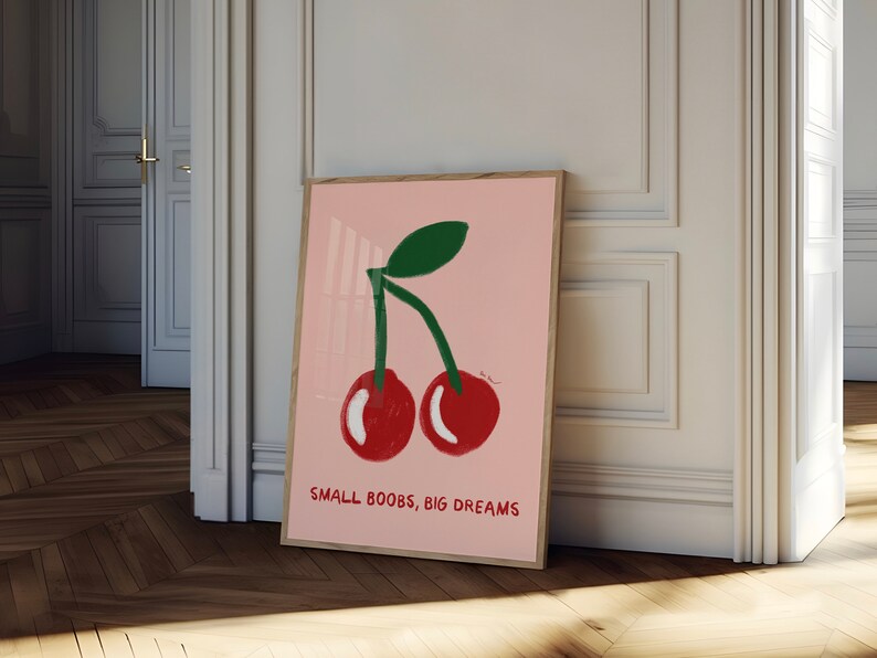 K&ouml;nnte beinhalten: Ein rosa Poster mit einer Grafik von zwei roten Kirschen mit gr&uuml;nen Stielen und Bl&auml;ttern. Der Text "SMALL BOOBS, BIG DREAMS" ist unter den Kirschen gedruckt.
