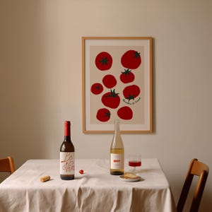 May include: A framed print featuring red tomatoes with green stems and leaves. A bottle of red wine, a bottle of white wine, a glass of red wine, and a small plate with bread are on a table covered with a white tablecloth.