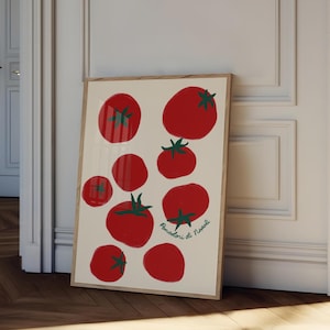 May include: A framed art print featuring a collection of red tomatoes with green stems on a cream background. The print includes the text "Pomodori di Napoli" in green script. The artwork is displayed against a white wall and a wooden floor.