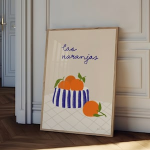 May include: A framed print with a light beige background featuring a blue and white striped bowl filled with orange oranges. The text "las naranjas" is written in purple above the bowl.