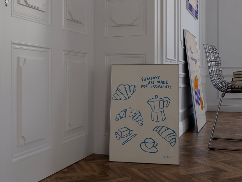 Op de afbeelding: Een witte poster met blauwe illustraties van croissants, een koffiepot en een kopje koffie. De tekst op de poster luidt "Zondagen zijn gemaakt voor croissants".