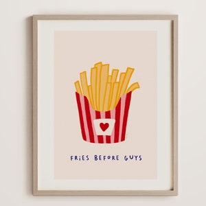 May include: A framed art print featuring a whimsical illustration of golden french fries in a red and white striped container with a heart. The text "FRIES BEFORE GUYS" is written in blue below the fries.