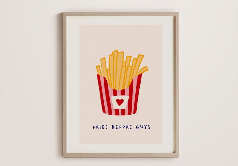 May include: A framed art print featuring a whimsical illustration of golden french fries in a red and white striped container with a heart. The text "FRIES BEFORE GUYS" is written in blue below the fries.