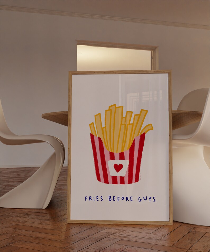 May include: A framed art print featuring a colorful illustration of a container of french fries. The fries are yellow, and the container is red and pink with a heart. The text "FRIES BEFORE GUYS" is written in blue.