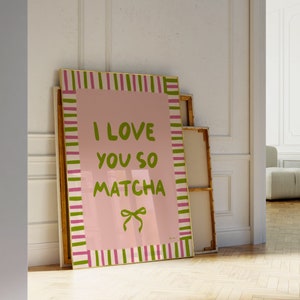 May include: A pink and white striped framed canvas with the text "I love you so matcha" in green lettering. The canvas is leaning against a white wall.