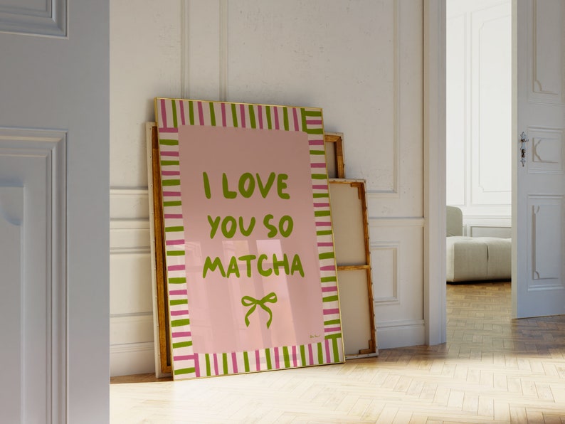 May include: A pink and white striped framed canvas with the text "I love you so matcha" in green lettering. The canvas is leaning against a white wall.