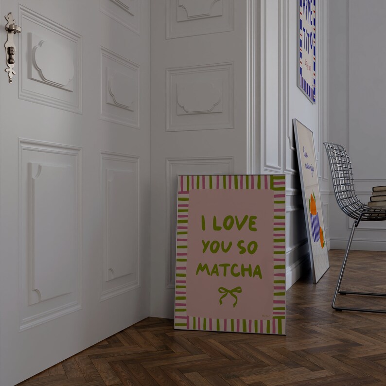 May include: A pink and green striped poster with the text "I love you so matcha" in green lettering. A small green bow is in the bottom right corner of the poster.