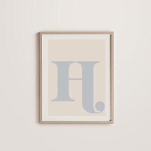 May include: A framed print featuring a light beige background with a large, grey letter "H" in a stylised font.