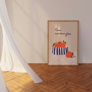 May include: A framed print with a blue and white striped bowl filled with orange fruit. The text "las naranjas" is written in blue above the bowl. The print is on a white background with a checkered pattern.