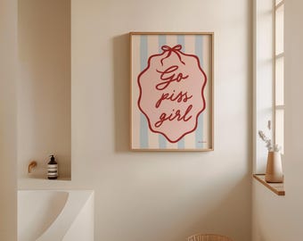 May include: A framed print with a pink and blue striped background. The print features a red oval with the text "Go piss girl" in a cursive font.