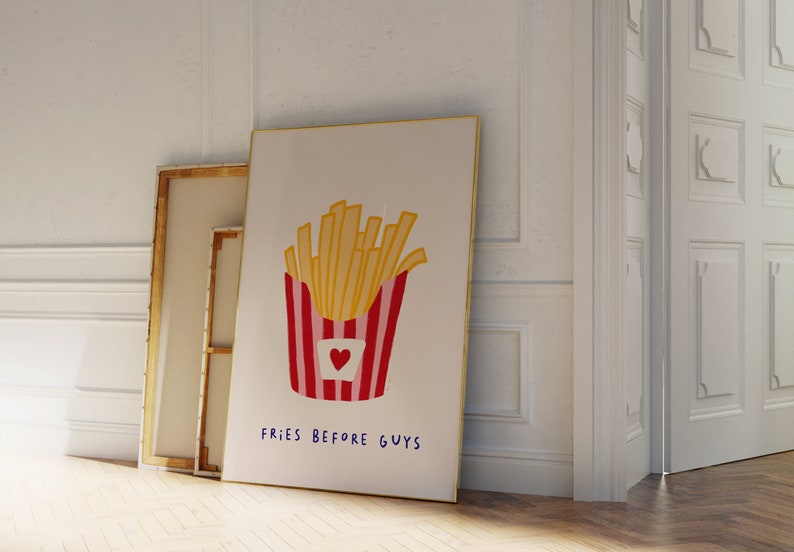 May include: A framed art print featuring a cartoon illustration of a container of french fries. The fries are yellow, and the container is red and white striped with a heart. The text "FRIES BEFORE GUYS" is written below.