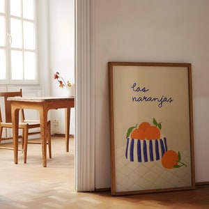 May include: A framed print with a white background and a blue and white striped bowl filled with orange oranges. The text "las naranjas" is written in purple cursive above the bowl.