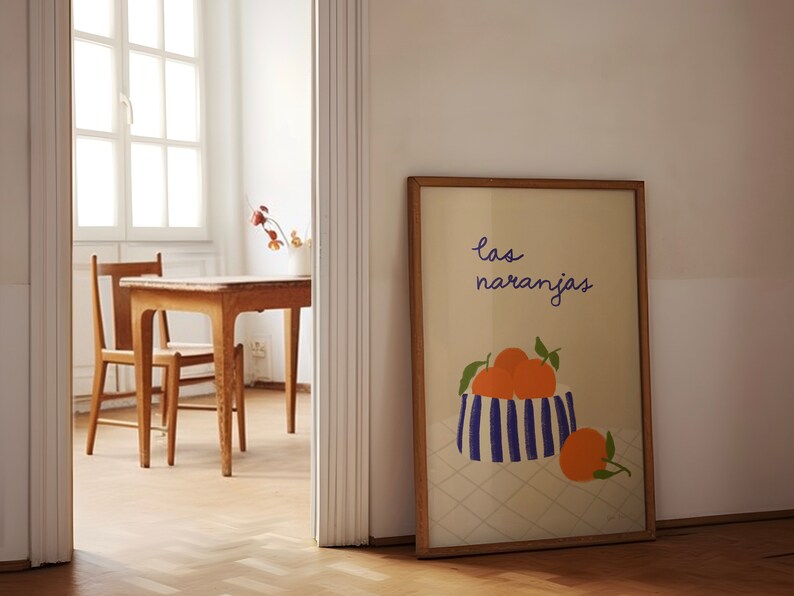 May include: A framed print with a white background and a blue and white striped bowl filled with orange oranges. The text "las naranjas" is written in purple cursive above the bowl.