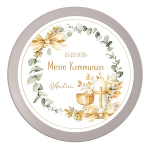 Könnte beinhalten: Ein runder, grauer Teller mit einem weißen Mittelteil, der ein Blumengirlanden-Design aufweist. Die Girlande enthält Eukalyptusblätter, goldene Schleifen und eine Kerze mit einem Kreuz. Der Text "Meine Kommunion" und der Name "Andrea" sind ebenfalls vorhanden.