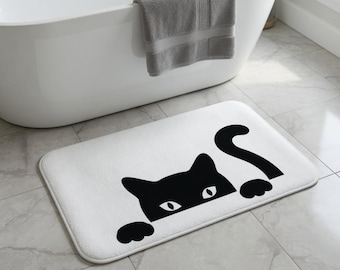 Peut inclure: Un tapis de bain rectangulaire blanc orné d'une illustration graphique noire représentant un chat qui regarde par-dessus le bord. Le motif du chat comprend deux oreilles pointues, deux yeux à pupilles blanches, deux pattes avant et une queue courbée.