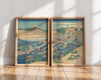May include: Two framed Japanese woodblock prints. One depicts Mount Fuji over a wavy sea, the other shows a river scene with figures and buildings. Both prints have a blue, green, and beige color palette.