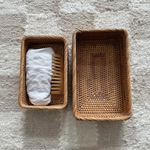 May include: Two woven wicker baskets, one containing a white towel and a wooden comb. The baskets are on a white fluffy rug.