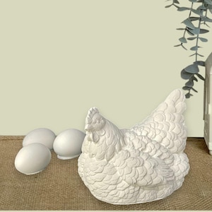 May include: White ceramic hen figurine with a detailed feathered texture, sitting on a burlap surface with three white ceramic eggs.