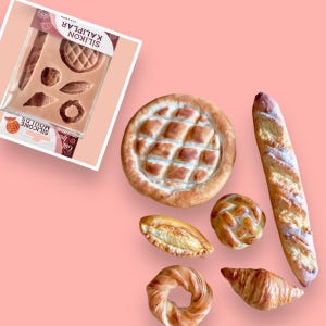 Può includere: Uno stampo in silicone per cuocere il pane, con una varietà di forme, tra cui una pagnotta rotonda, una baguette e un croissant. Lo stampo è mostrato con diversi prodotti da forno, tra cui una pagnotta rotonda, una baguette, un croissant, un anello di pane intrecciato e una piccola pagnotta di pane.