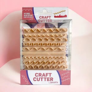Può includere: Una confezione di plastica trasparente contenente più lame per taglierina artigianale beige a motivi. La confezione ha un'etichetta rosa e bianca con le scritte "Craft Cutter" e "Patterned Ruler Cutters". Le lame hanno vari disegni dei bordi.