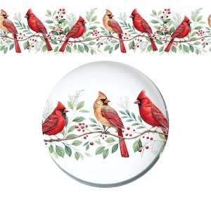 Op de afbeelding: Een ronde glazen presse-papier met een aquarelillustratie van felrode kardinaalvogels zittend op dunne bruine takken met groene bladeren en kleine rode bessen. Hetzelfde vogel- en bladerpatroon herhaalt zich in een horizontale rand erboven.