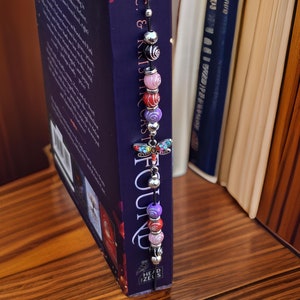 May include: A book with a black and purple beaded bookmark featuring a dragonfly charm. The bookmark reads "FOUND" on it.