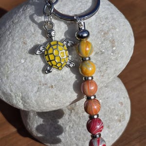 May include: A silver key chain with a yellow turtle charm and a colourful beaded dangle. The beads are yellow, orange, red and white with a swirl pattern.