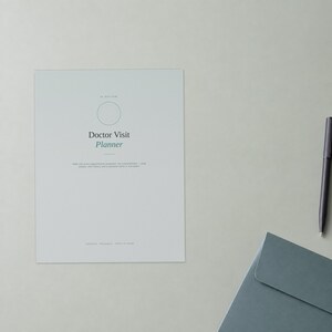 May include: A light grey Doctor Visit Planner document featuring a thin circular outline, black text, and green accent text. The document includes the title Doctor Visit Planner and smaller descriptive text. A black pen and a blue envelope are nearby.