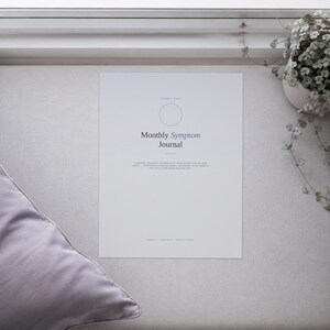 May include: A white rectangular Monthly Symptom Journal with a thin circular outline at the top. The text reads Monthly Symptom Journal followed by a small paragraph of descriptive text and the words UNDATED, REUSABLE, PRINT AT HOME at the bottom.
