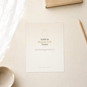 May include: A rectangular paper tracker with a cream background featuring the text ADHD & Hormone Cycle Tracker in black and brown font. The design includes a thin circular outline at the top and small printed text below the main title.