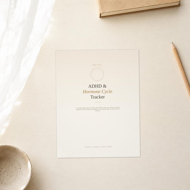 May include: A rectangular paper tracker with a cream background featuring the text ADHD & Hormone Cycle Tracker in black and brown font. The design includes a thin circular outline at the top and small printed text below the main title.
