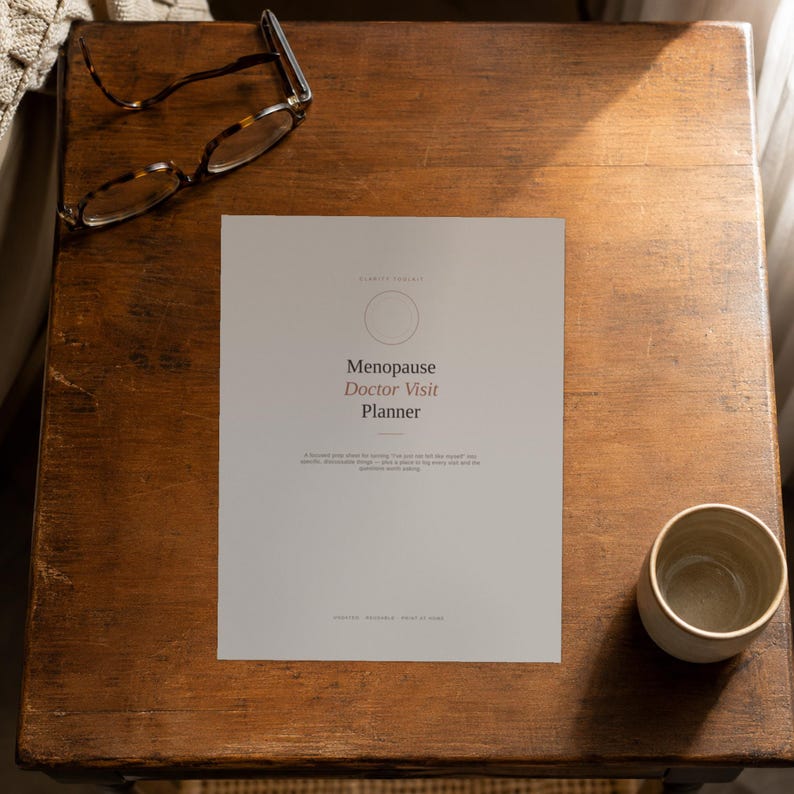 May include: A white paper sheet titled Menopause Doctor Visit Planner with a circular icon, accompanied by tortoiseshell spectacles and a small ceramic cup. The text includes a subtitle and a brief description of the planner's purpose.