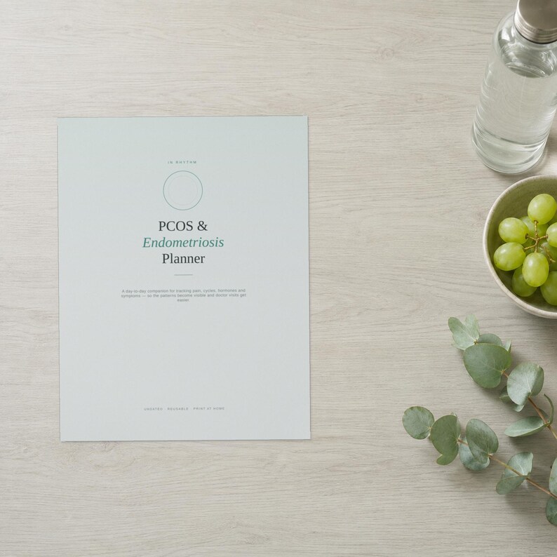 May include: A light grey planner with a circular outline and the text PCOS & Endometriosis Planner printed in dark grey and green. The cover includes a subtitle and small text at the bottom, presented in a clean, minimalist layout on a flat surface.