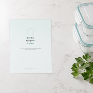 Może przedstawiać: Jasnoniebieski papierowy dziennik zatytułowany Food & Symptom Journal z okrągłą ikoną na g&oacute;rze. Tekst brzmi: A three-week food and symptom log to help your own connection between diet, inflammation and pain. Jest przeznaczony do druku w domu.