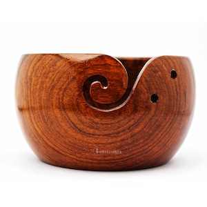 May include: A wooden yarn bowl with a spiral design and three holes. The bowl is a rich reddish-brown color.