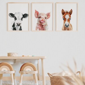 以下が含まれることがあります： 農場の動物を描いた水彩画が3枚、額装されています。絵は、牛、豚、子馬です。絵は、白い壁に、木製のテーブルと2脚の木製の椅子の上に飾られています。