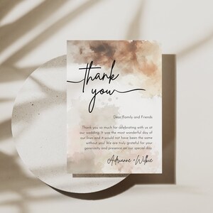 May include: A watercolor thank you card with a brown and pink background. The text reads "Thank you" in a handwritten font. The text below reads "Dear Family and Friends" and includes a message of gratitude for celebrating the couple's wedding. The card is signed "Adrianne & Wilkie".