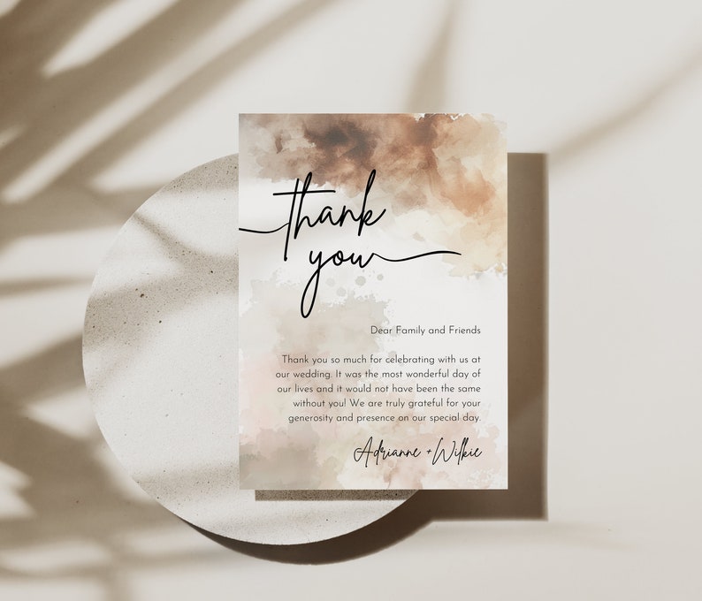 May include: A watercolor thank you card with a brown and pink background. The text reads "Thank you" in a handwritten font. The text below reads "Dear Family and Friends" and includes a message of gratitude for celebrating the couple's wedding. The card is signed "Adrianne & Wilkie".